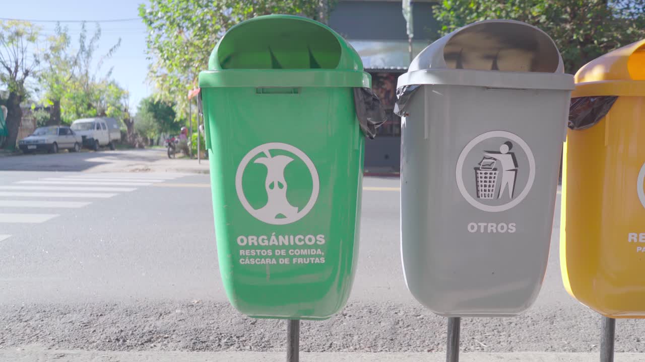 Colorful recycling bins on the sidewalk of a road in a rural village.