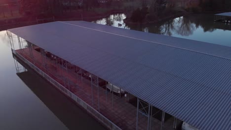 Aerial-view-of-lake-and-boat-docks-flying-upwards-to-see-land-and-water-all-around-with-sunset-in-the-background