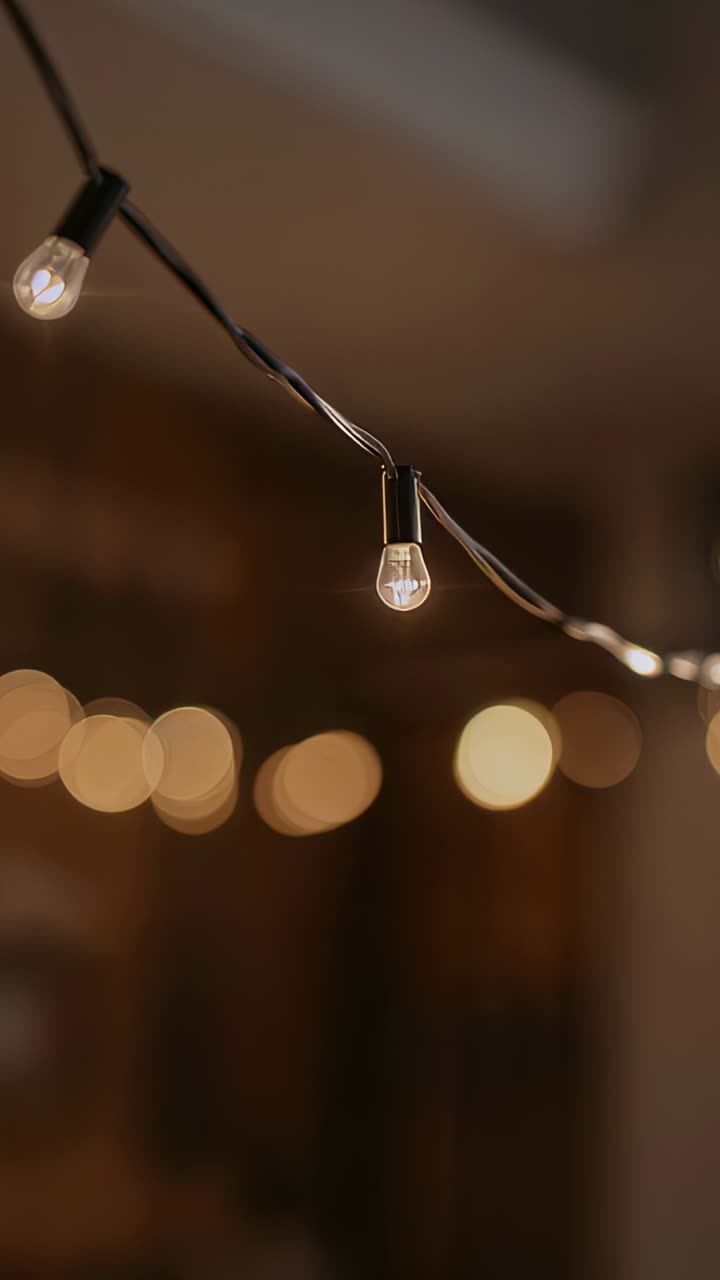 Vertical video: Camera panning over hanging clear bulbs on porch, capturing warm mood and dark wire