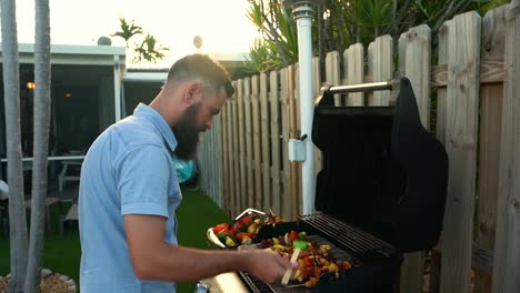 caucasian male basting chicken, steak, vegetable shish kabob skewers on backyard grill