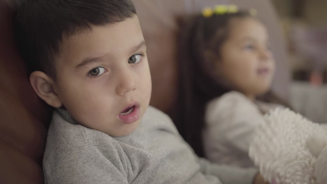 Primo piano del viso di un bambino mediorientale seduto con sua sorella sul divano.