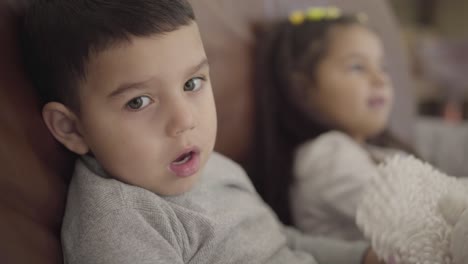 close-up face of a little middle eastern boy sitting with his sister at the coach