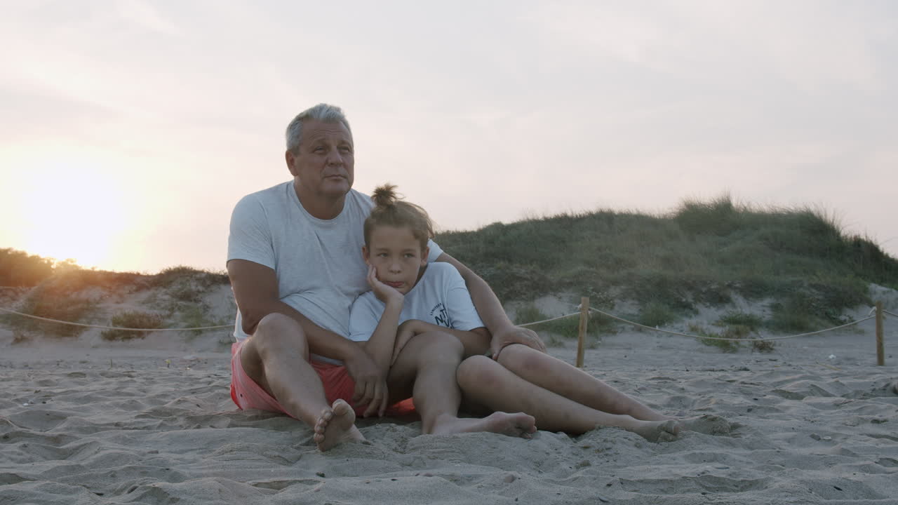 Bedstefar og barnebarn på stranden ved solnedgang.