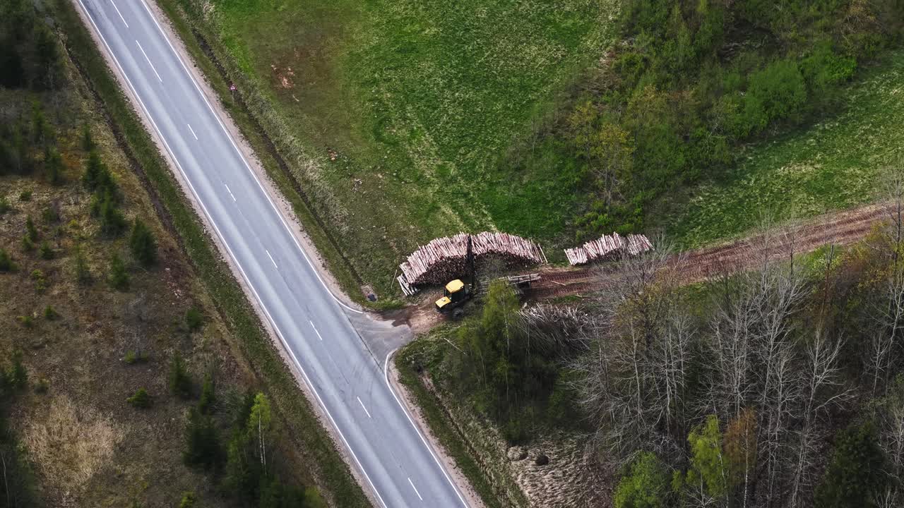 Drone descending through trees to reveal forest harvester operating on green terrain