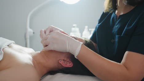 medium view of spa visitor upper lips smoothed by beauty technician wearing protective gloves with gentle fingertip massage under clinical lamp evoking professional care and relaxation