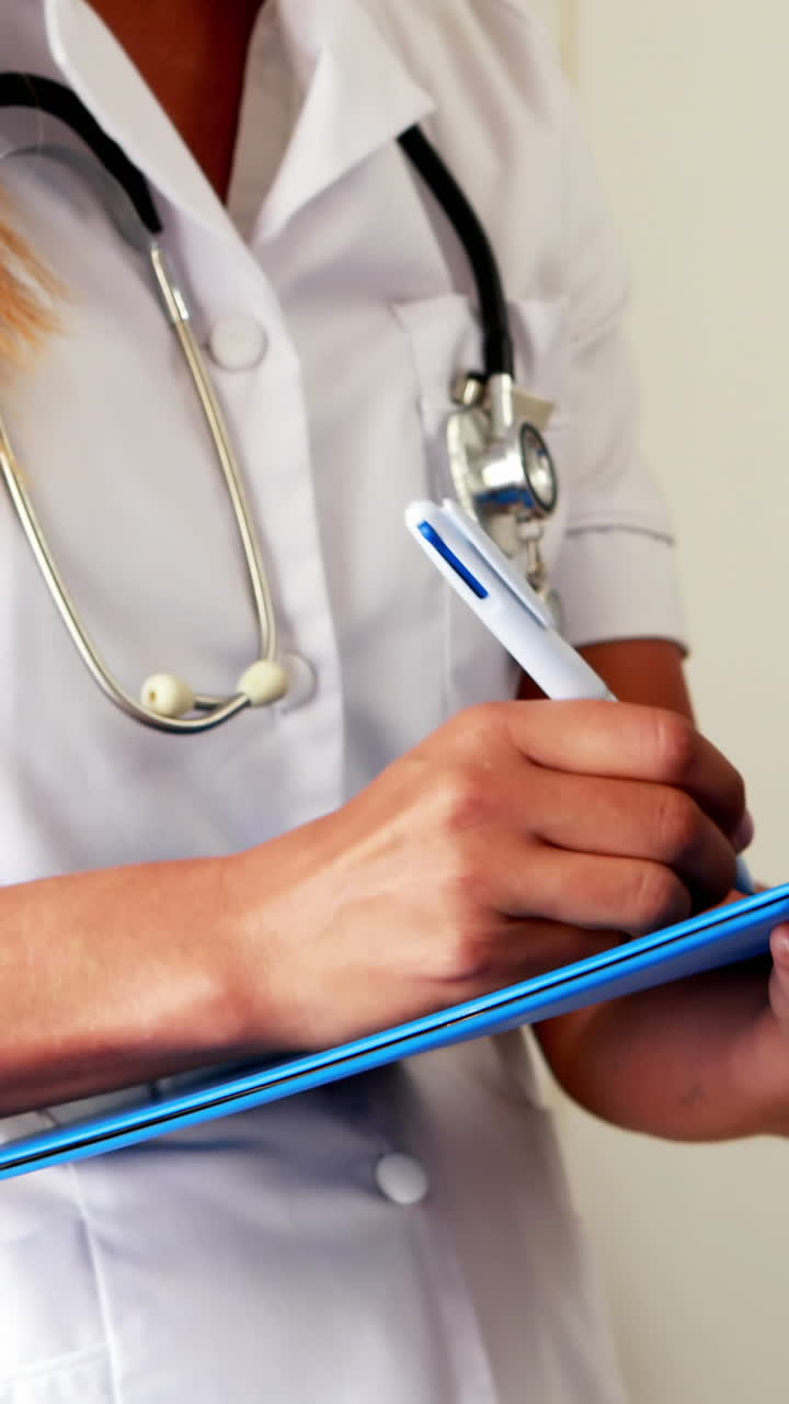 médico femenino con un estetoscopio escribiendo en un cuaderno mientras está de pie
