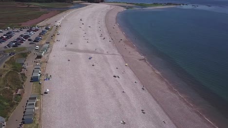 volando sobre la playa de budleigh, en el suroeste de inglaterra, donde la gente disfruta de un día al aire libre sentada en la playa de guijarros.
