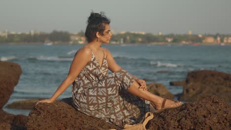 A-woman-sitting-on-rocks-near-a-calm-beach-looking-longingly-into-the-distance