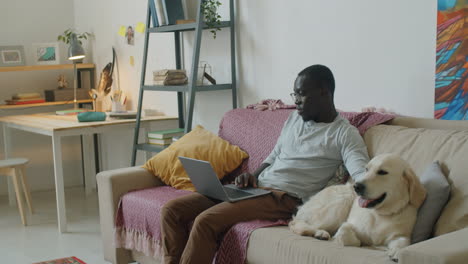 Black-Man-Using-Laptop-and-Petting-Dog-on-Sofa