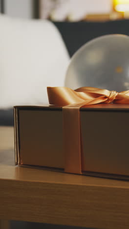 vertical video of present in gift wrapped box decorated with ribbon on table in lounge with balloon