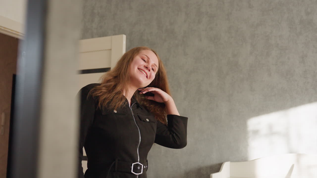 검은색 드레스를 입은 모델이 자신감 넘치게 방으로 걸어 들어가 따뜻한 미소를 지으며 우아하게 회전해요. 햇빛이 비쳐 그녀의 모습이 빛나고, 자연스러운 매력과 분위기를 풍기며 스타일리시하고 우아하게 움직여요.