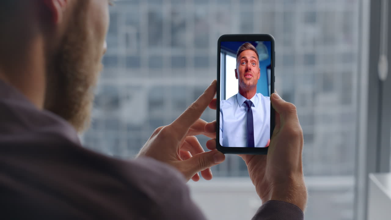 Videochiamata di un uomo d'affari con telefono cellulare in ufficio, primo piano. Manager che guarda lo schermo