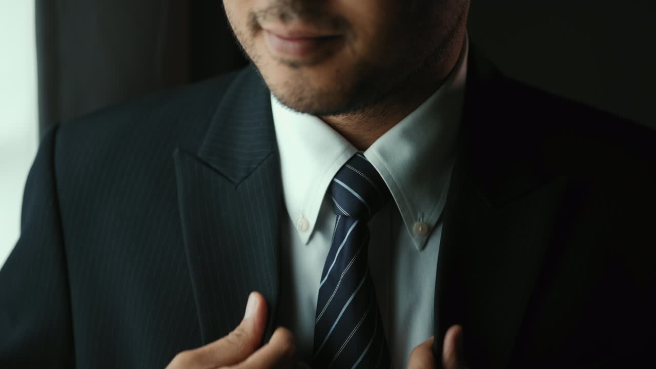 hombre de negocios confiado en traje azul clásico atando o ajustando corbata cerca de la ventana en la habitación del hotel por la mañana. hombre guapo con un buen traje en el día de la boda.