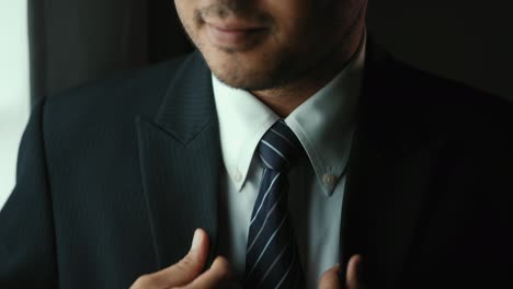confident businessman in classic blue suit tying or adjust necktie near window in hotel room at the morning. handsome man wearing a nice suit on wedding day.