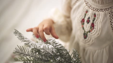 Zeitlupenaufnahme-Eines-Jungen-Mädchens,-Das-Einen-Kiefern-Weihnachtszweig-In-Einem-Weißen-Festlichen-Kleid-Streichelt---Nahaufnahme