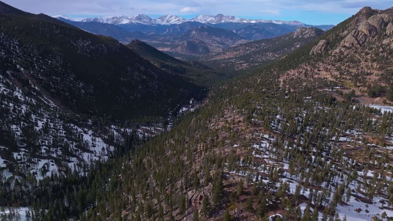 Long mountain ridgeline stretching into hazy distance with snow traces and alpine vegetation, high angle aerial pullback, Allenspark Colorado USA