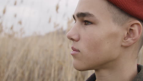 Close-Up-View-Of-A-Teenage-Boy-With-Orange-Beanie-And-Plaid-Coat-Looking-At-Side-In-A-Wheat-Field,-Then-Looks-At-Camera-And-Smiles-1