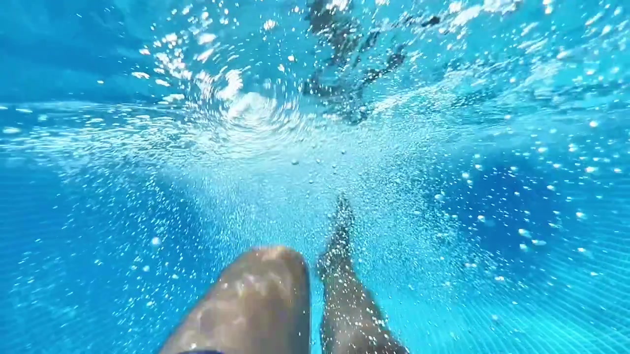 Angolazione della telecamera POV che mostra le gambe di un nuotatore che scalciano sott'acqua con bolle d'aria che circondano l'inquadratura. Ottimo per promozioni di vacanze estive, sport, resort e fitness acquatico.