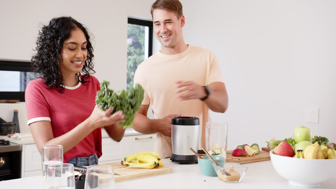 Preparing healthy smoothies, young multiracial couple chopping fruits and vegetables, at home