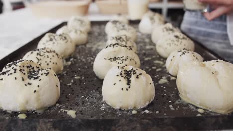 asian baker working in bakery kitchen, sprinkling poppy seeds on rolls in slow motion