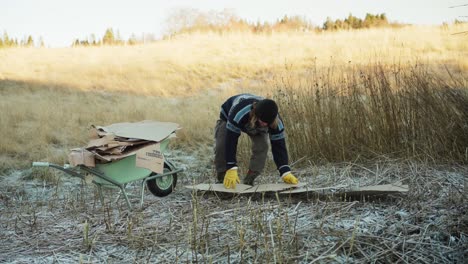 a man is getting the cardboard ready for use as mulch, and his dog accompanies him - static shot