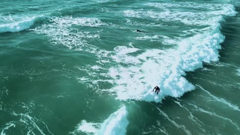 a drone shot of a surfer catching a small wave, surfing towards the shoreline