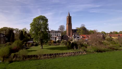 Backwards-aerial-movement-revealing-Dutch-painterly-picturesque-meadows-and-agrarian-area-at-the-edge-of-a-village-town-showing-wider-countryside-surrounding