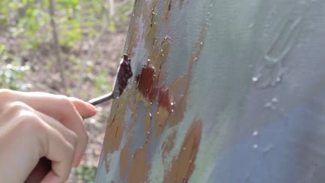 professional female artist uses palette knife to create texture on multicolored abstract painting with red paint outside during the day, camera tilt up