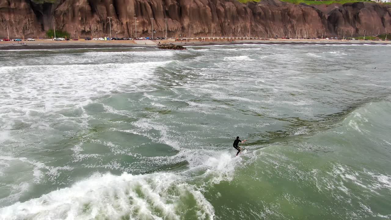 video aéreo diurno de 4k siguiendo a un surfista montando una ola en las aguas costeras del océano pacífico en lima, capital del perú