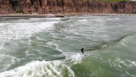 4k-daytime-aerial-video-following-a-surfer-riding-a-wave-on-the-coastal-waters-of-the-Pacific-Ocean-in-Lima,-capital-city-of-Peru