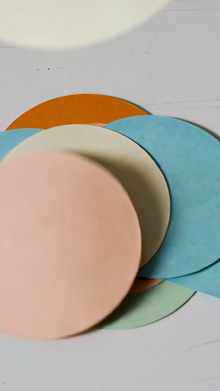 Vertical video: Entering blue disc causing hand stacking pastel discs on pale table forming fan