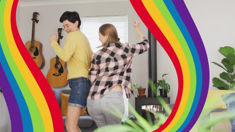 animation of pride rainbow bands over happy caucasian lesbian couple dancing at home