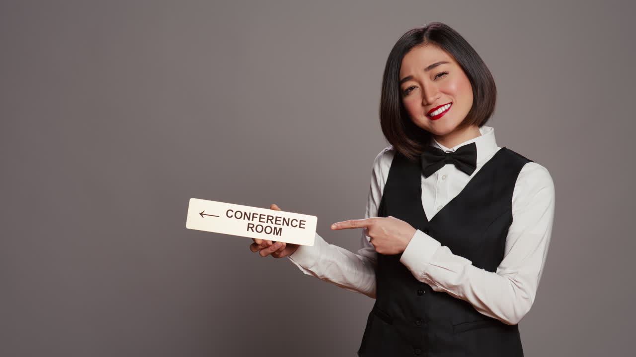 recepcionista asiática señalando el indicador de pared para la sala de conferencias