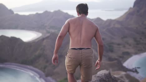 man is enjoying the view of nature on top of a hill without a shirt on