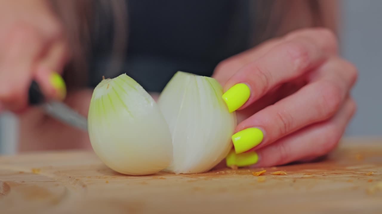 Slow motion macro careful onion cutting with neon nails highlighting contrast