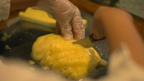 Freshly-peeled-yellow-pineapple-fruit-being-cut-into-long-slices-on-metal-chopping-board,-filmed-in-slow-motion-as-over-the-shoulder-close-up-shot