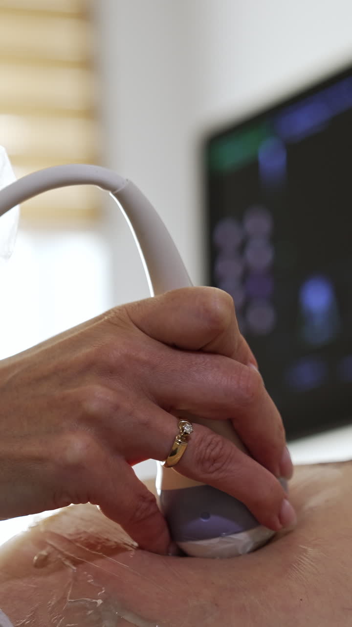 Ultrasonic diagnostic for pregnant lady. Doctor is moving the transducer by the patient's abdomen in the hospital. Close up. Black screen at backdrop in blur.