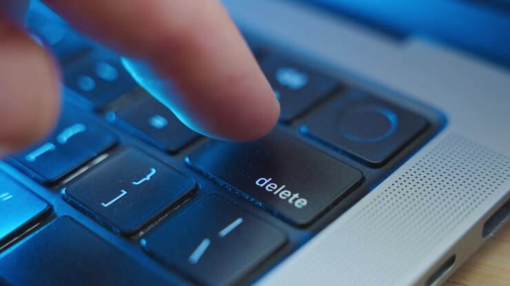 Close up on finger pressing the Delete keypad on laptop computer keyboard in office or home. Dark room at night as person erases files from system or cleaning data. Urgent removal by hacker or user