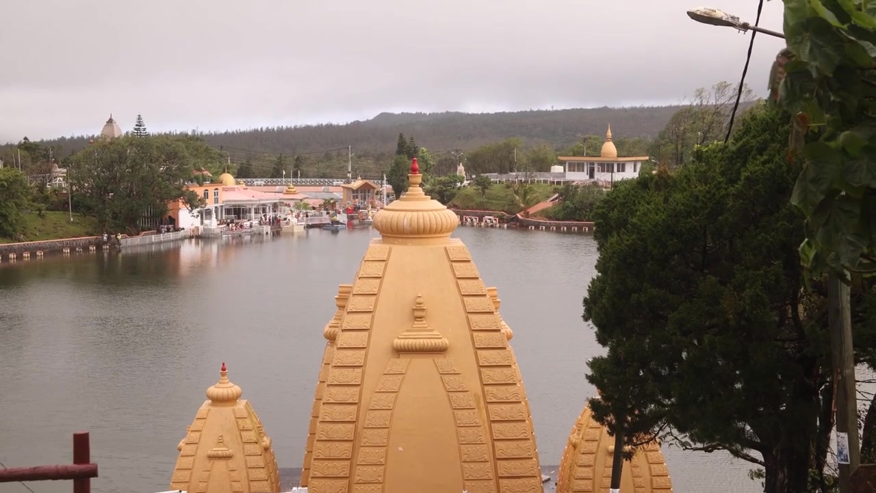 Gyldne arkitektoniske kupler af det hinduistiske tempel ved Ganga Talao, Grand Basin, Mauritius, der reflekteres blødt på det hellige søvand i dagslys