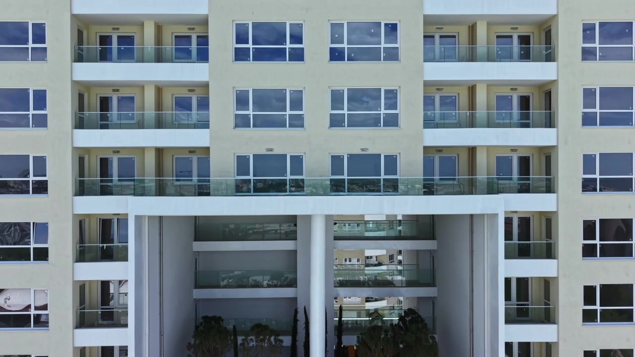 Vista de um jardim na varanda em um edifício moderno com paredes de vidro e árvores, localizado em uma área urbana durante o dia.