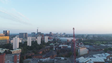 drone moves past a construction crane in a cityscape of birmingham, uk at sunset with clear skies