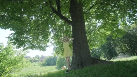 woman in yellow dress dancing by tree in summer park