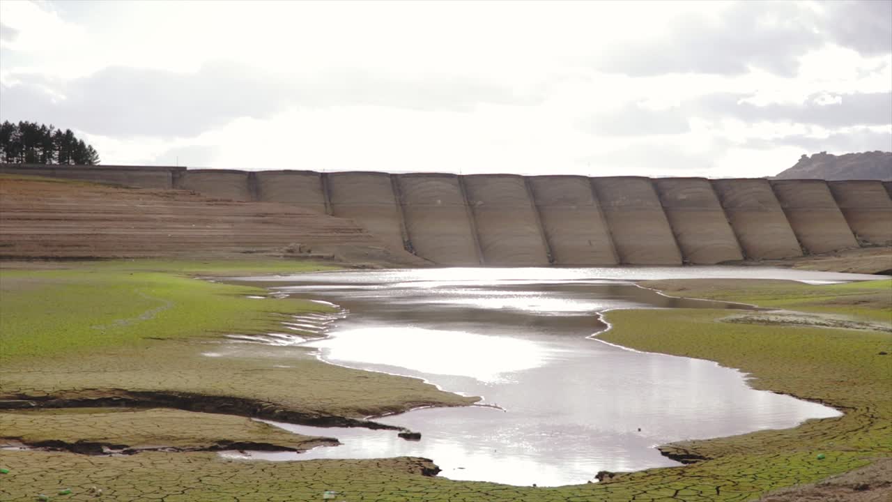 Lake and dam and little water in the drained out basin of the lake caused by drought in a cloudy autumn day.