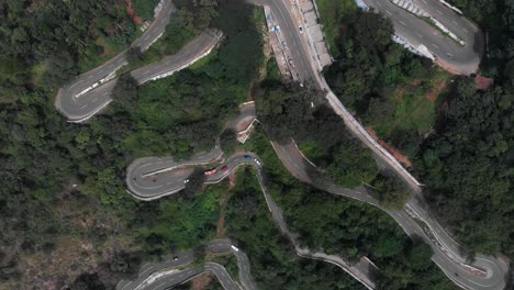 Hairpin-bends-in-Yercaud,-India-covered-with-endless-vast-green-forest-with-trees-growing-rapidly-vehicles-passing-on-the-road