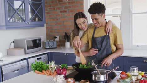 feliz pareja biracial cocinando juntos y riendo en la cocina