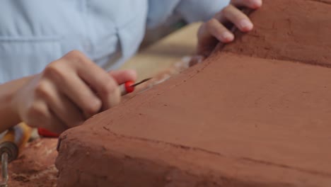 close up of woman automotive designer's hands using rake or wire to create details in the sculpture of car clay in the studio