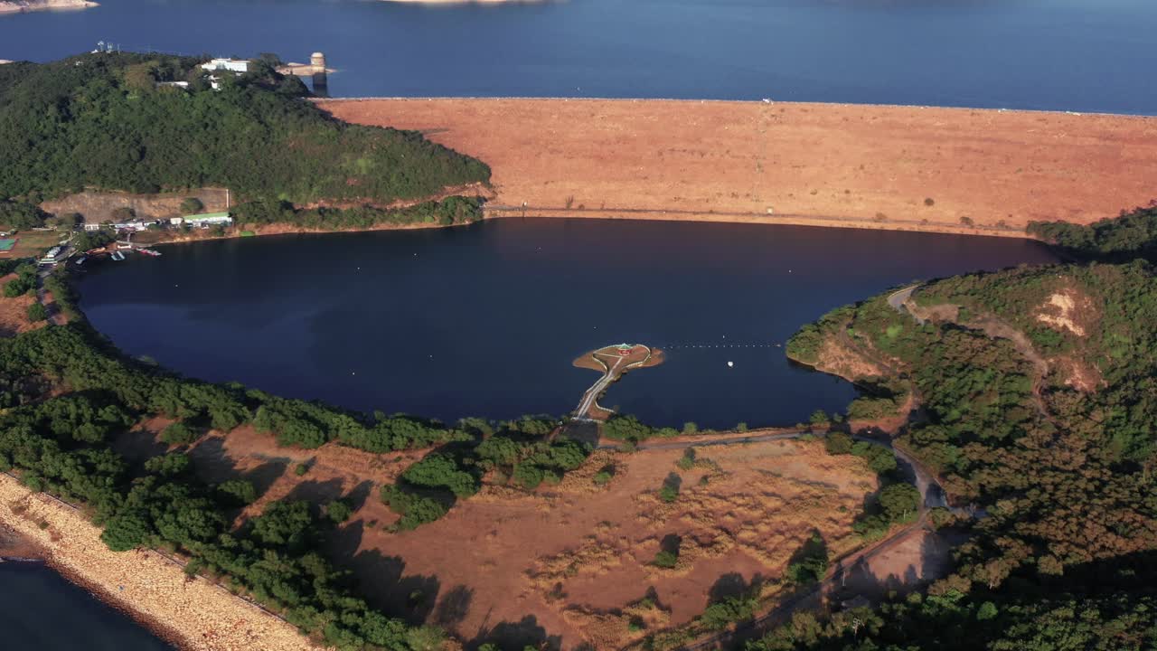 Aerial view of a beautiful reservoir created by the dam and a small village on the bank of the reservoir in Hong Kong Geographical Park in Sai Kung on a sunny day
