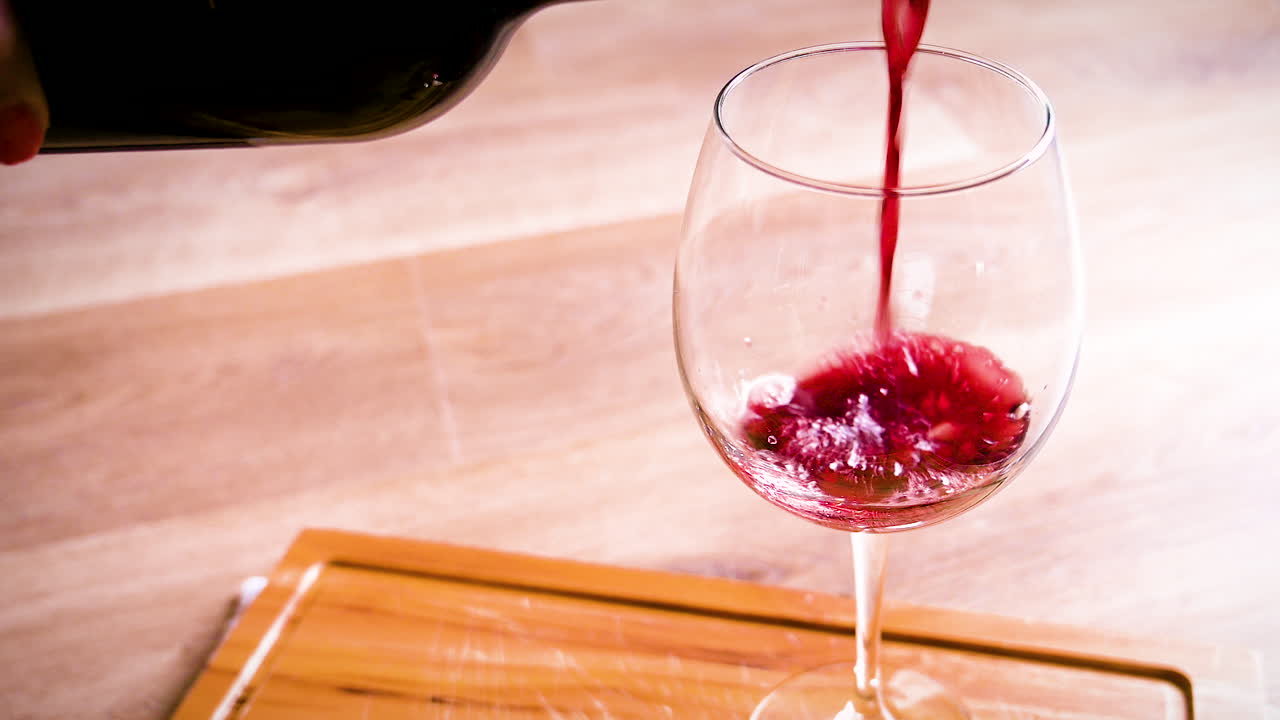 Versare vino rosso nel bicchiere sullo sfondo di legno