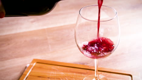 Pouring-red-wine-into-the-glass-against-wooden-background