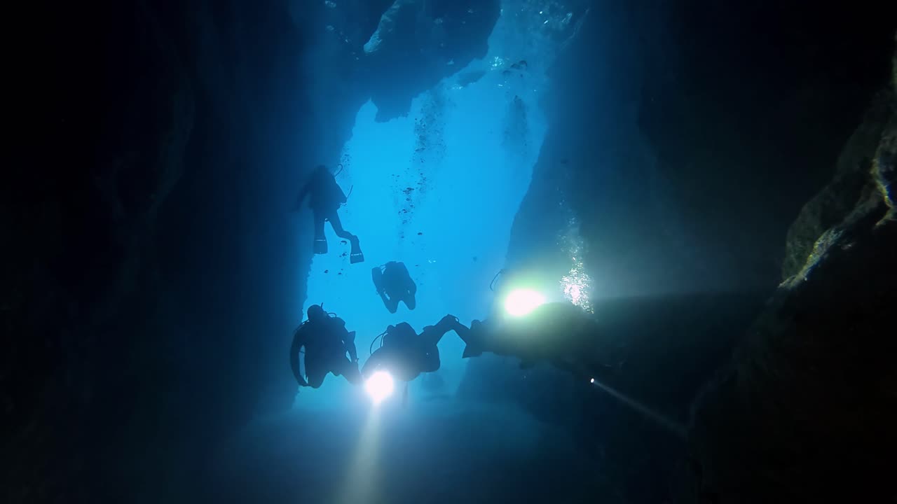 Mysterious Deep Sea Exploration by Group of Scuba Divers Silhouetted Against Radiant Blue Light in Submerged Rock Cave Tunnel of Mediterranean Gozo Malta During Clear Summer Day Low Angle Perspective
